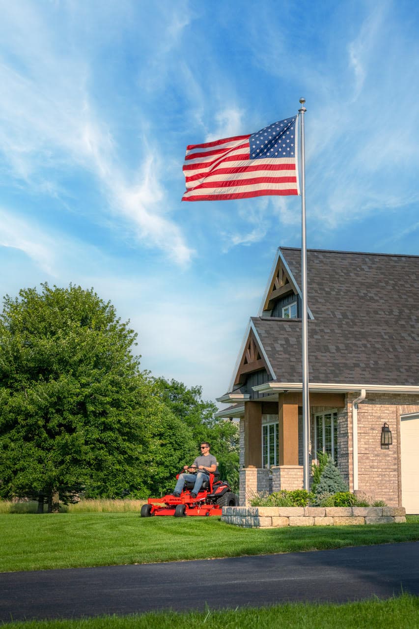 An American flag flying above a lawn care professional mowing a property